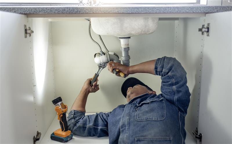 Plumber repairing pipes beneath a bathroom sink in Clermont