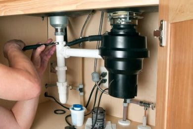 Plumber repairing a garbage disposal beneath a kitchen sink in Clermont