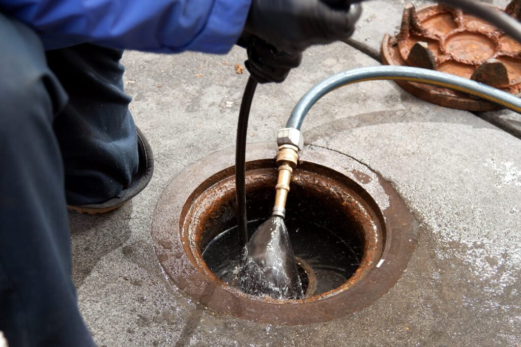 Plumber hydro jetting a sewer line through a manhole in Clermont