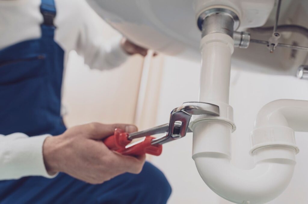 Plumber repairing a white drain pipe beneath a sink in Clermont