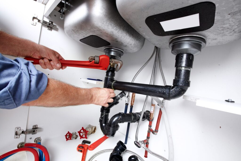 Plumber repairing drain pipes beneath a kitchen sink in Clermont